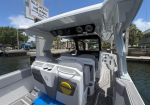 Rear cockpit of a white speedboat with an open canopy, two captain chairs, rear seating, a built-in cooler and yellow speaker, at a marina.