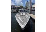 Front-on view of a sleek gray-and-white speedboat tied to a marina dock, with urban buildings in the background under a sunny sky.