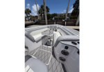 White and gray boat cockpit with U-shaped seating and a pedestal-mounted folding table; marina and palm trees visible in the background.