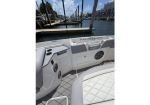 White boat cockpit with built-in controls and seating, at a marina with docks and buildings in the background.