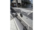 Boat cockpit with gray cushioned seating and a built-in speaker, overlooking a marina with boats and buildings in the distance.