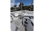 White and gray boat cockpit with U-shaped seating around a pedestal table, built‑in speakers, and a diamond‑pattern deck at a sunny marina.
