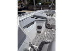 White boat cockpit with a cushioned helm seat, built-in speakers, and storage compartments, docked at a marina.