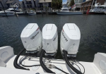 Three white outboard motors mounted on the stern of a boat at a marina with other boats in the background.