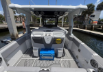 Rear view of a modern gray boat docked at a marina, with a blue cooler on the deck under a white hardtop helm console