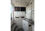 Interior of a compact control cabin in a service vehicle with storage drawers and control panels above a small counter and sink area.