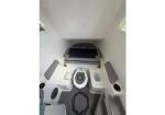 Compact marine head: white restroom aboard a boat with a central portable toilet and built-in storage surrounding it, in a narrow cabin.
