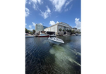 White motorboat gliding through a marina with modern buildings and a bright blue sky above.