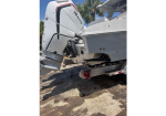 White motorboat on a trailer with its outboard motor raised, parked on a dirt lot; palm trees in the background.