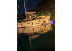 White luxury yacht moored at night with calm water and reflected lights on the surface behind it.