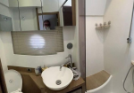 Small bathroom with a round white sink on a wooden counter, mirrored cabinets above, and a person visible in the reflection of the mirror taking the photo.