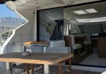 Open yacht interior with a teak table on deck, white seating, and sliding doors to the cabin and helm area behind.