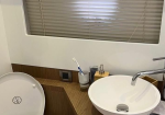 Bathroom vanity with a white round vessel sink, chrome faucet, toothbrush in a holder, soap dispenser, and a window with closed blinds behind.