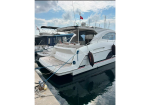 White motor yacht docked at a marina with fenders along its side and a Turkish flag flying from the mast, blue sky above and calm water nearby.