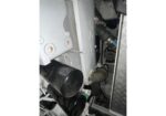 Close-up of industrial machinery with white panels, black cylindrical components, and metal diamond-plate flooring in a cramped engine bay.