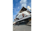 White motor yacht on dry dock supported by stands, with brown fenders along the hull and people nearby under a blue sky.
