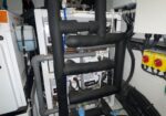 Insulated black pipes and a white control panel clutter a mechanical room with yellow safety switches nearby