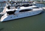 White luxury yacht docked at a marina, with a wooden pier and other boats in the background.