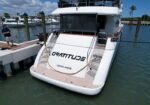 Rear view of a white luxury yacht named Gratitude docked at a marina; a man stands on the pier with a remote control nearby.