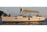 White sailing yacht with three people aboard on calm blue water, sails furled and deck crew visible.