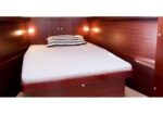 Wood-paneled cabin with a compact bed, white mattress, striped pillow, and built-in storage drawers nearby.