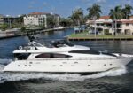 White luxury motor yacht cruising along a canal with palm-lined waterfront homes in the background.