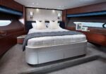 Luxurious yacht cabin with a large bed, white bedding, gray throw, and decorative pillows amid wood-paneled walls and built-in side tables.