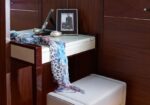Wood-paneled vanity area with a cream cushioned stool, scarf draped over the edge, and a framed photo on the countertop.