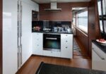 Modern yacht galley with white cabinets, stainless steel oven, gas cooktop, and wood paneling.