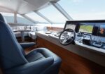 Yacht cockpit with a leather captain's chair, steering wheel, and several navigation screens along a wood-paneled console.
