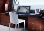 White chair at a dark blue vanity desk on a yacht, with a framed mirror, photo frame, and makeup items, ocean view outside window