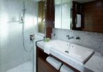 Modern bathroom featuring a glass-enclosed shower, a white rectangular sink, and a marble countertop with folded towels beneath. Adaptive lighting and mirrored cabinets add a spacious feel.