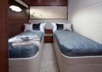 Twin-bedded yacht cabin with blue patterned duvets, white pillows, wood paneling, and a central nightstand.