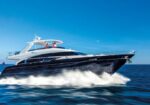 Black luxury motor yacht speeds over blue water, leaving a white wake under a clear sky.