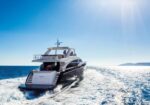 A sleek luxury yacht speeds through bright blue ocean, leaving white wake under a sunny, clear sky.