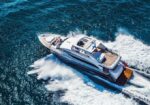 A luxury motor yacht speeding through blue ocean, white wake trailing behind it from a high-angle view