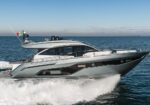 Sleek silver-gray luxury motor yacht speeding across blue ocean with white wake behind it.