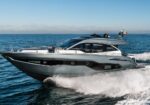 Luxury motor yacht speeding across the open sea, creating a white wake behind it under a clear blue sky with an Italian flag on the stern rail.