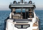 Rear view of a white luxury motor yacht on calm blue water, open aft deck with seating and a wooden swim ladder to the upper deck (Cranchi logo visible)