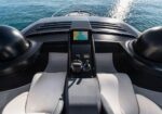 Center console of a luxury speedboat with a navigation display, steering wheel and throttles, water in view ahead.