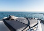 Luxurious yacht sunbed area with dark cushions and pillows on a clear day, calm sea in the background and a safety railing.