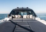 Top deck of a luxury yacht with a large gray sunbed and a cushioned seating area, facing the calm blue sea.