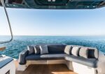 Luxurious outdoor lounge on a boat with gray cushions and pillows, overlooking calm blue sea under a clear sky.