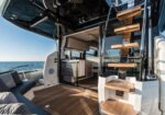 Luxurious yacht deck with open living area, wooden stairs, and ocean view on a sunny day