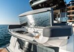 Backyard cockpit of a white luxury yacht with a built-in grill, chrome rail, and dark cushioned seating overlooking the ocean.