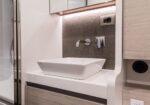 Modern bathroom vanity with white rectangular vessel sink, wall-mounted faucet, and textured brown backsplash with under-cabinet lighting.