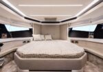 Luxurious yacht cabin with a large round bed, cream upholstery, and curved built-in seating along porthole windows.