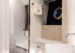 Contemporary bathroom with a glass-enclosed shower, white sink, and light wood wall panels.