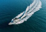 Overhead view of a white speedboat racing across deep blue water, leaving a frothy wake behind.