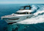 White luxury motor yacht speeding across calm blue sea with a wake behind.